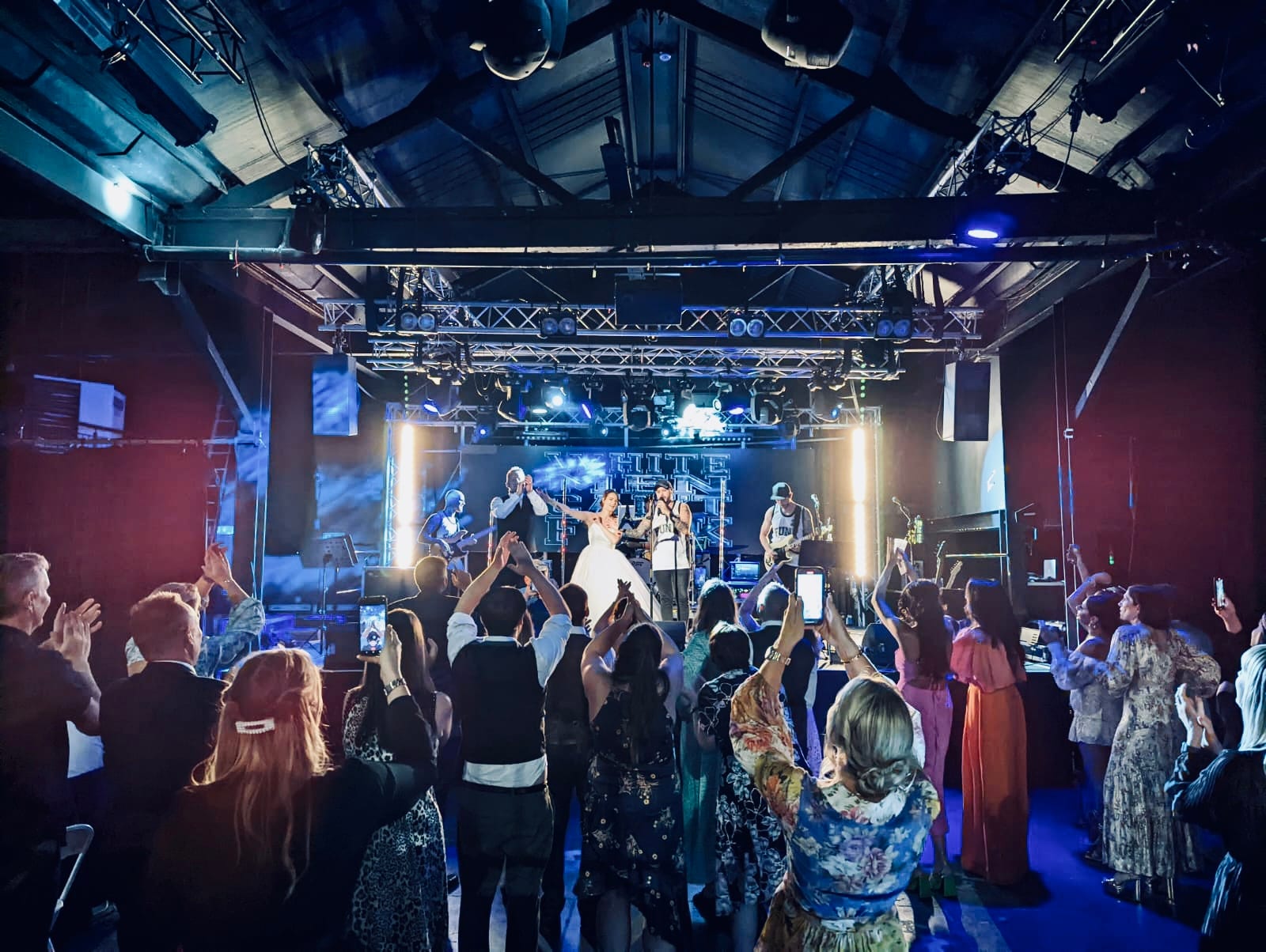A packed crowd with hands in the air in front of the lit stage