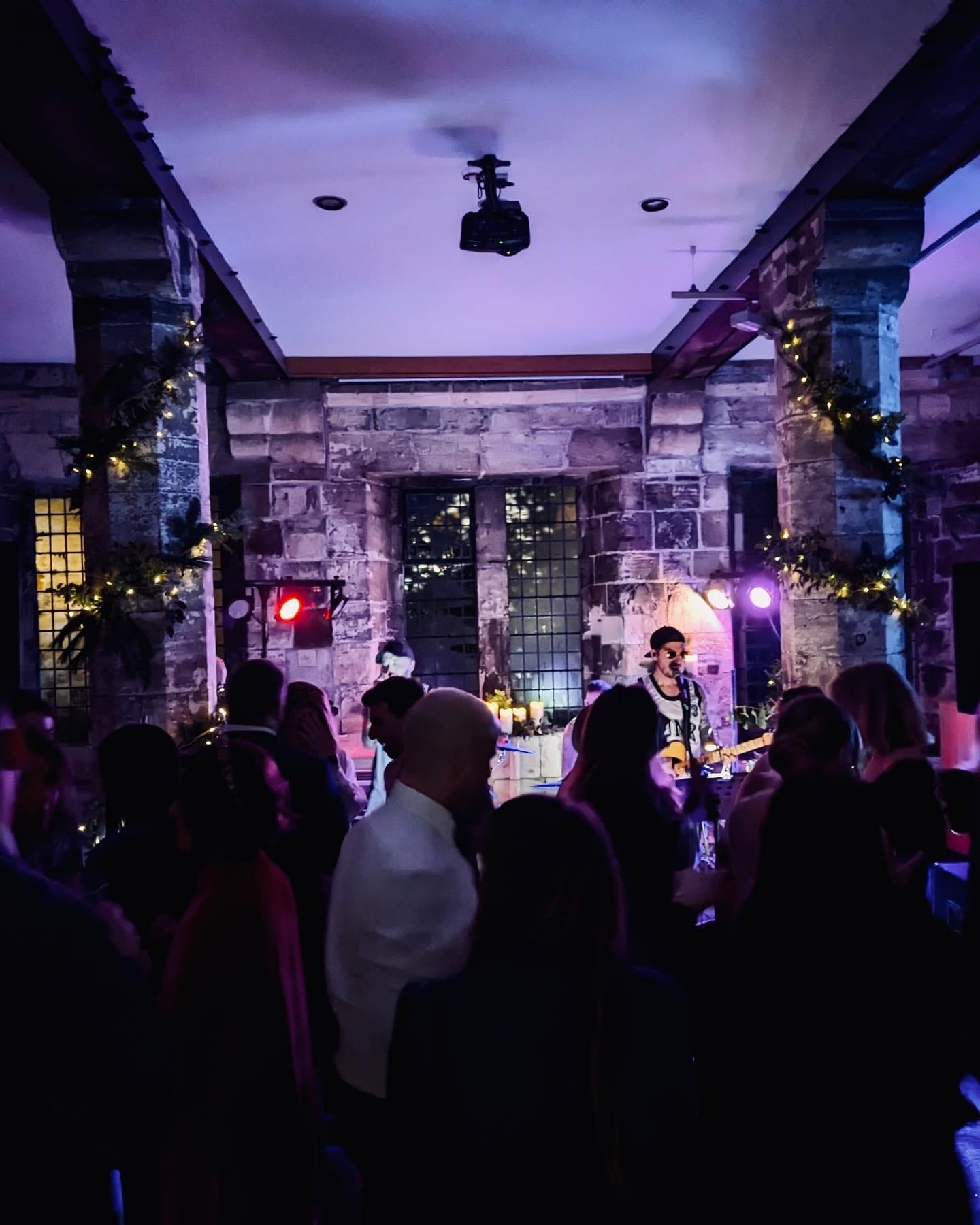 The singer performing in a stone-walled venue, guests close around him