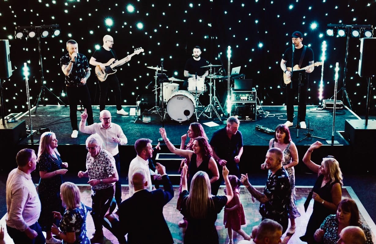 The band on a lit stage seen from above, the dancefloor packed in front of them