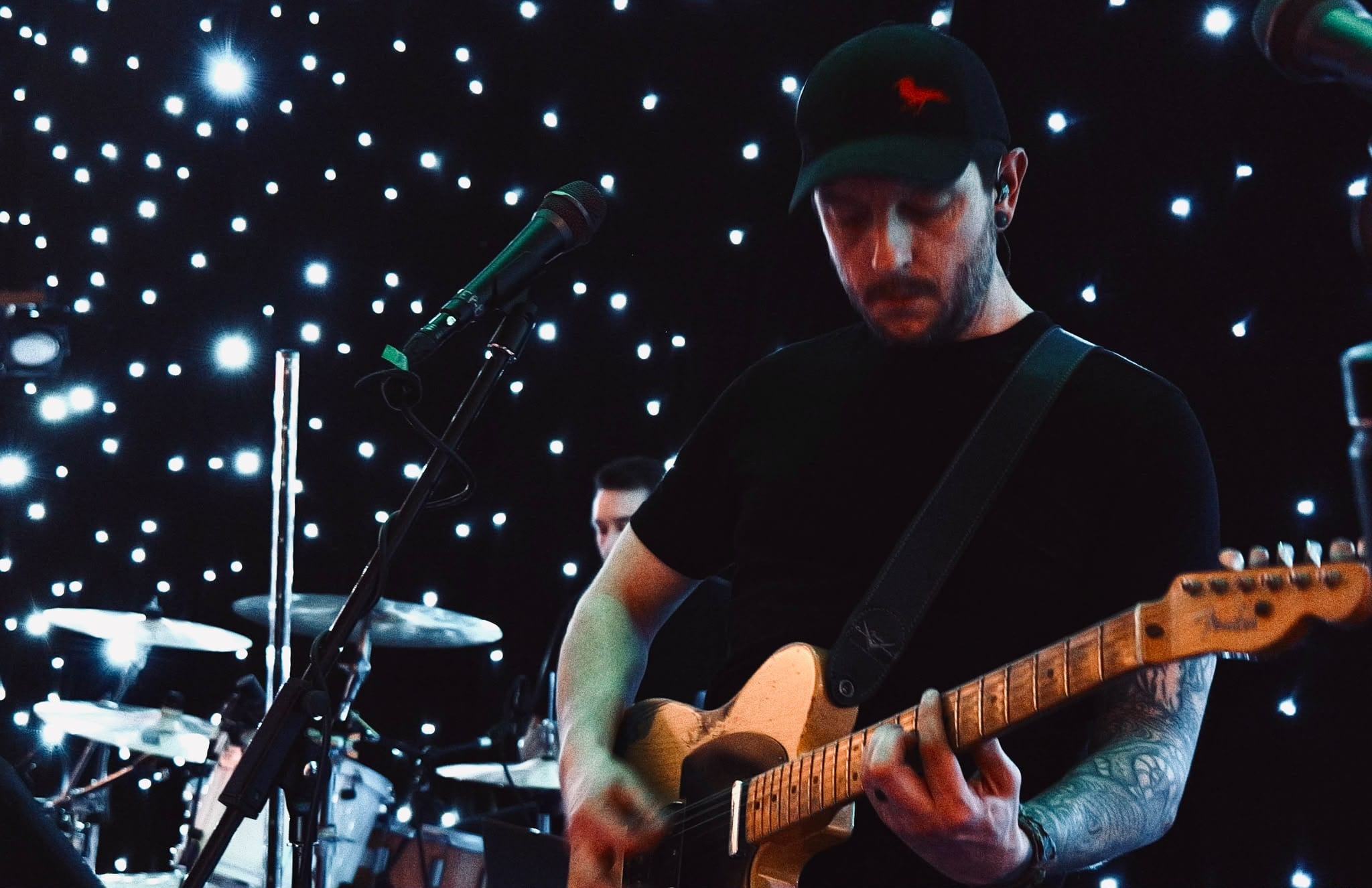The guitarist playing a Telecaster in front of a star-lit black backdrop